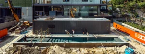 a couple standing in front of a sleek, modern container pool surrounded by construction materials and workers, showcasing the complexity and labor involved in installation.